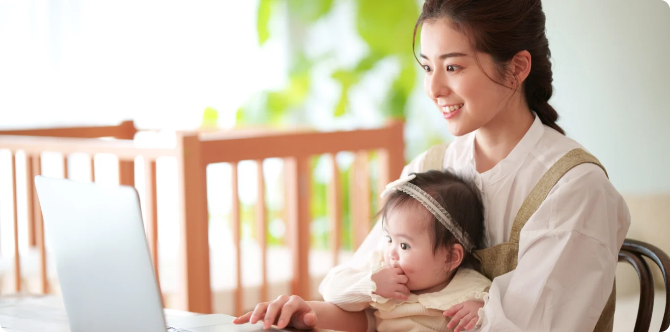 子供を膝の上に乗せながらパソコンで仕事をする母親の写真